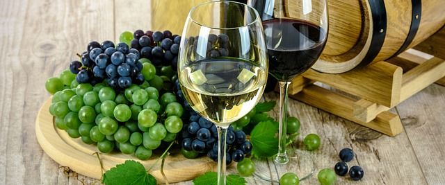 Zwei Gläser Wein neben Trauben und einem kleinen Holzfass