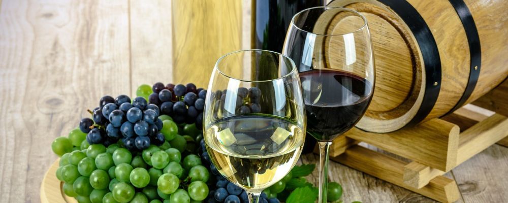 Zwei Gläser Wein neben Trauben und einem kleinen Holzfass